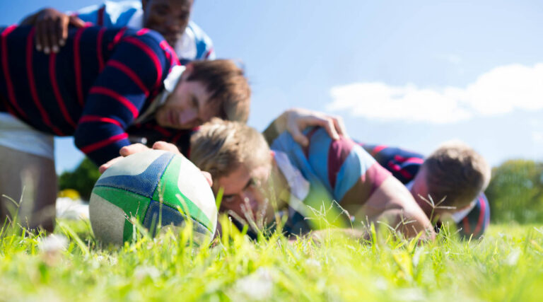 close up of men playing rugby while lying at grassy field on sunny day